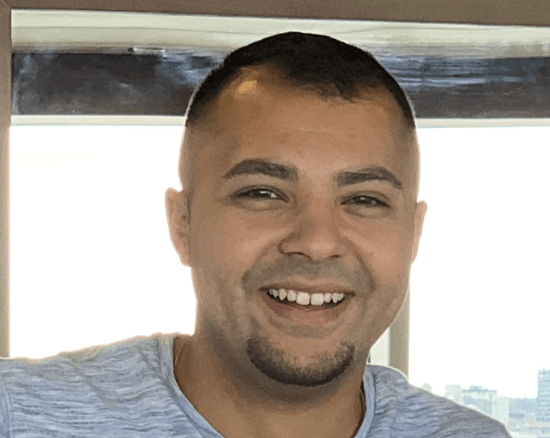 A smiling man with a faded haircut and goatee looks directly at the viewer.