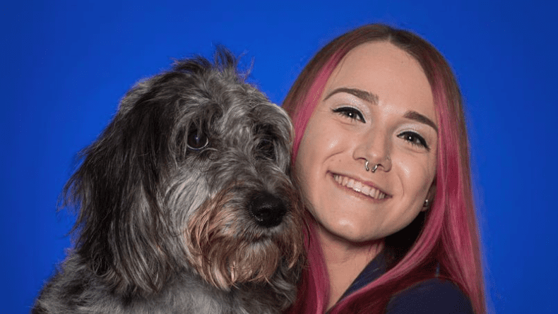 A smiling woman with pink hair and a nose ring poses closely with her scruff