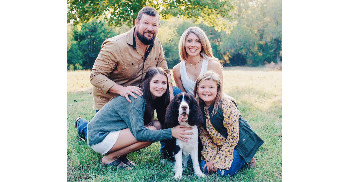 Smiling family of four with their black and white Springer Spaniel dog outdoors.