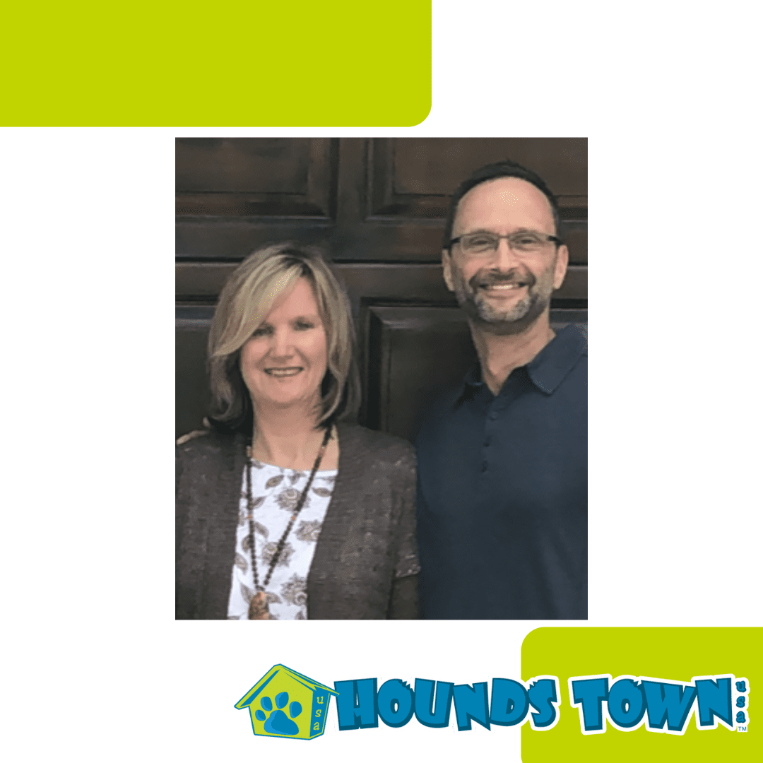 A smiling man and woman stand together in front of a wooden door, with the