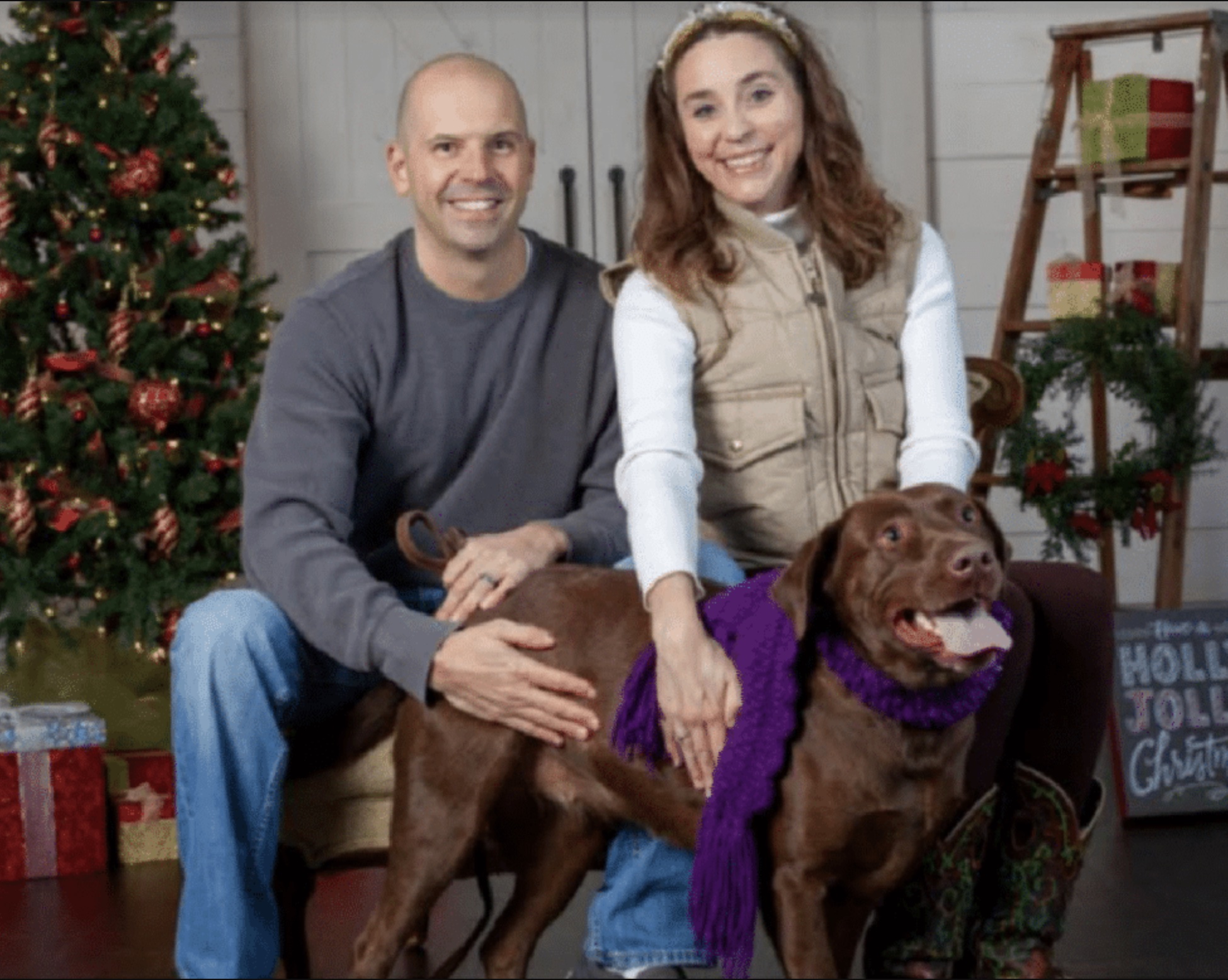 Smiling couple with their brown Labrador dog wearing