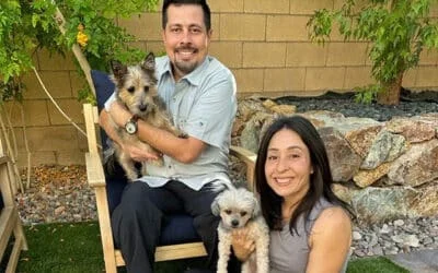 Smiling couple holding two small dogs in a backyard