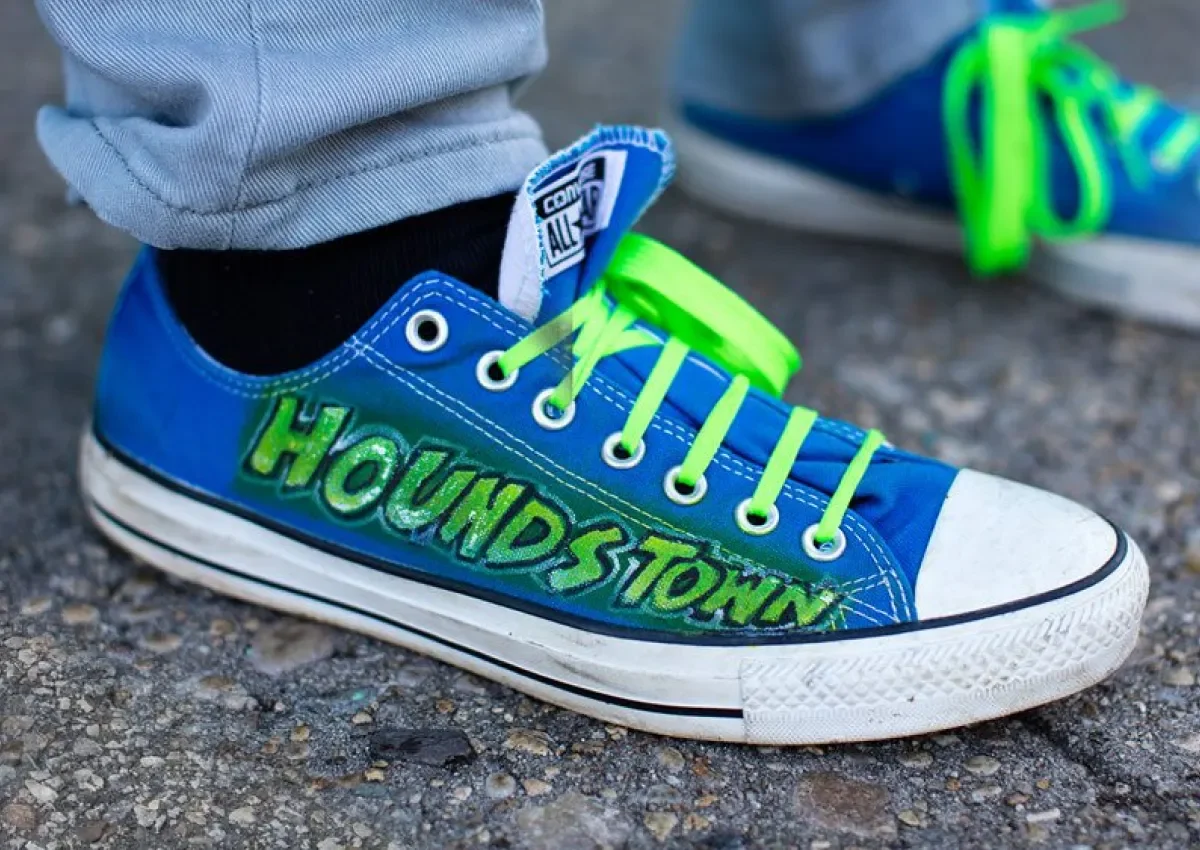Colorful blue sneaker with neon green laces and "Houndstown" written on the side, set against a pavement background.