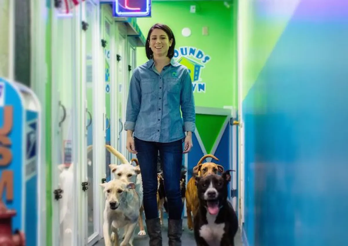 A woman walking with several dogs in a colorful dog daycare hallway.